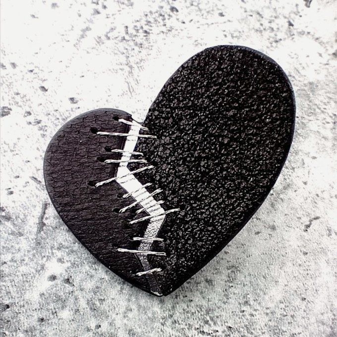 Zoom sur une boucle d'oreille Résilience : coeur fendu raccommodé en cuir noir et argent