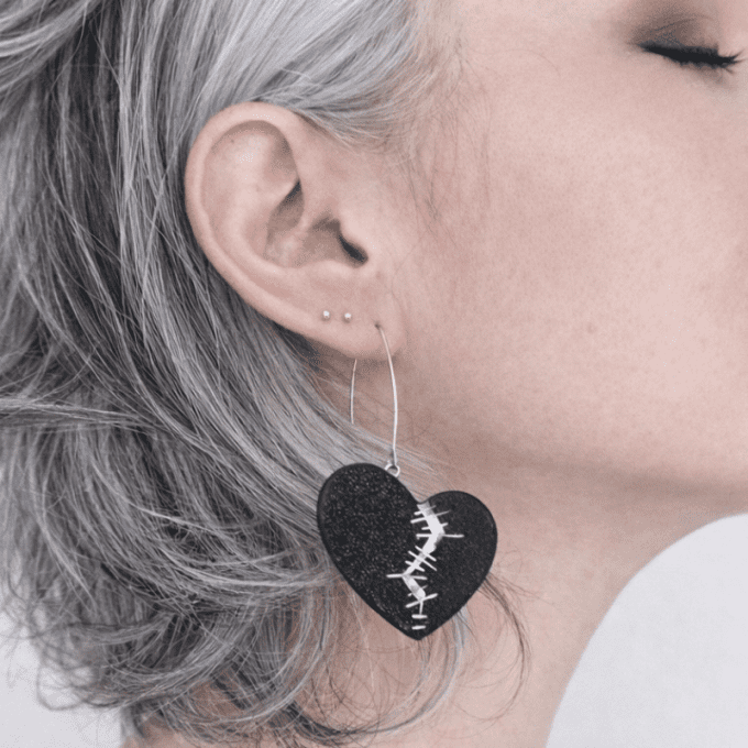 Boucle d'oreille Résilience : coeur fendu recousu en cuir noir et argent portée