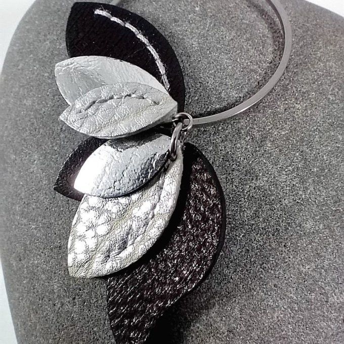 Gros plan sur la boucle droite en cuir noir, argent miroir et argent mat, suspendue à un anneau en i