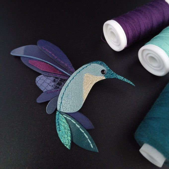Broche colibri multicolore en cuir, vue de face : reflets turquoise, verts, bleus et violets, découp