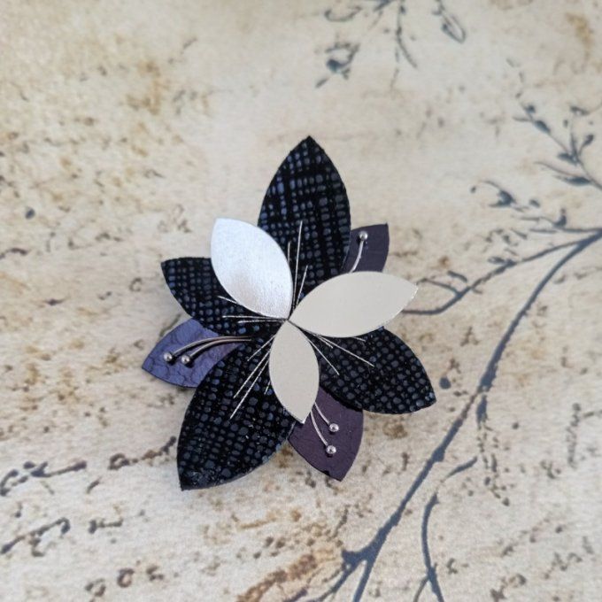 Broche fleur Luna Bloom Nuit Marine en cuir bleu et argent, posée sur un fond poétique à écritures e