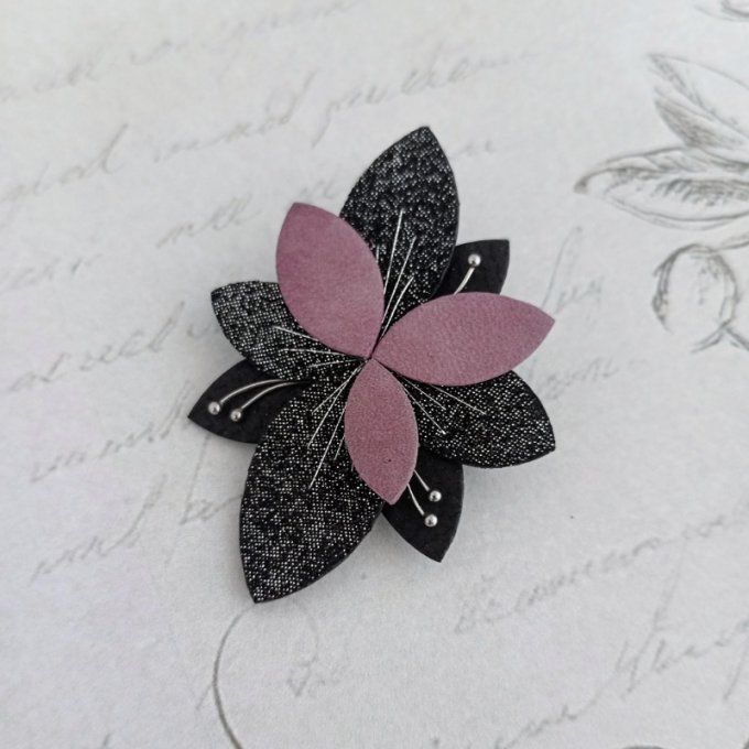 Broche Luna Bloom en cuir rose et noir brodé main de fil argenté, posée sur un fond romantique