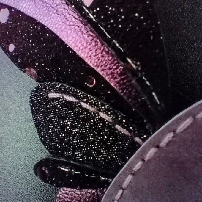 Zoom sur les plumes du colibri en cuir noir pailleté et roses, montrant la découpe et les coutures